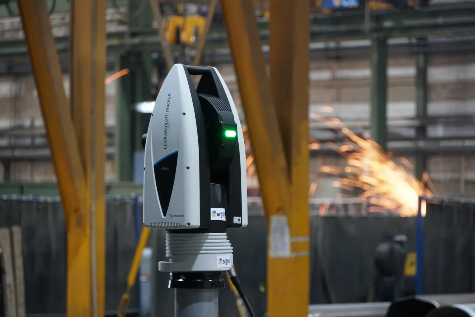 Leica Absolute Tracker ATS600 i en produksjonshall med gnister fra sveising i bakgrunnen