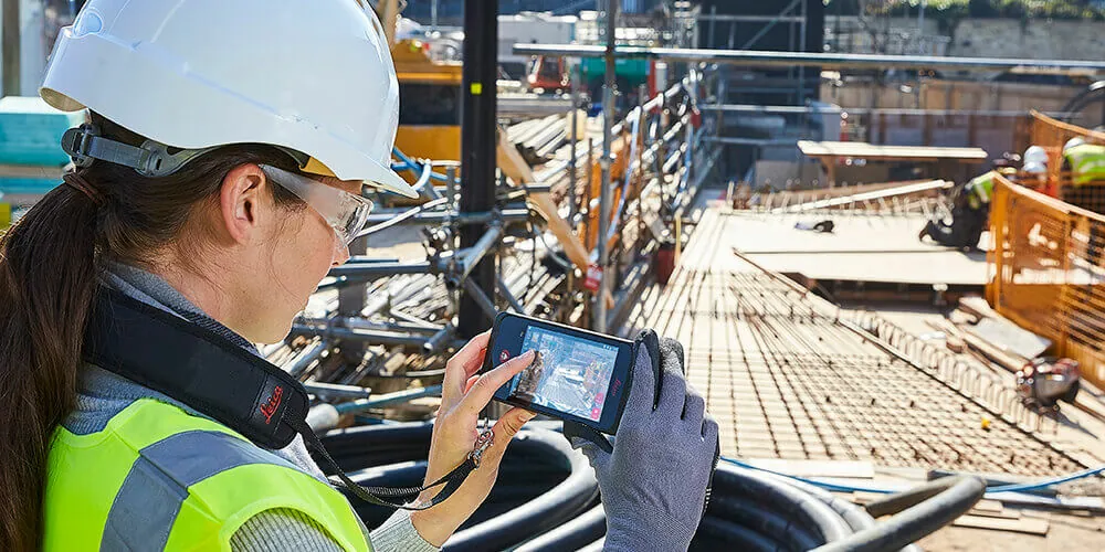 Kvinne med hjelm og refleksvest måler i et bilde på Leica BLK3D på en byggeplass