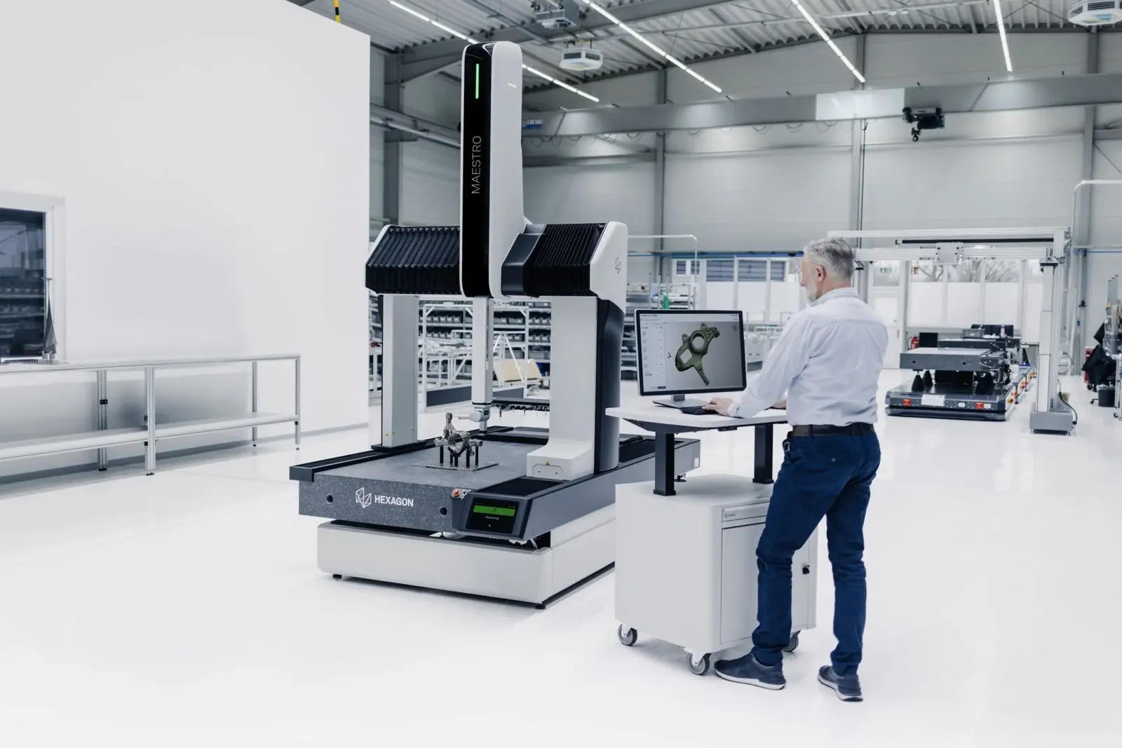 Operatør ved Hexagon MAESTRO koordinatmålemaskin som måler en del, med CAD-modell på skjermen